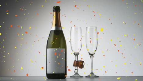 confeti cayendo sobre una botella de champán y dos vasos de champán contra un fondo gris