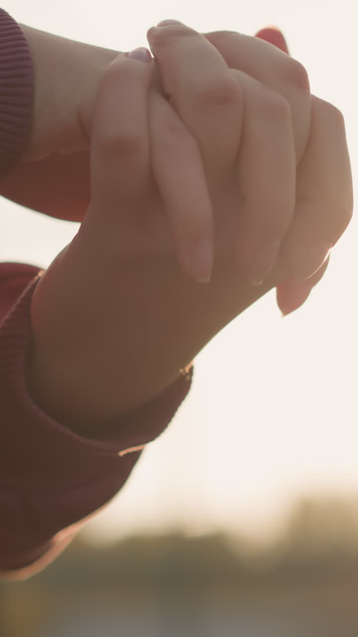 은색 옷을 입은 여성의 손이 손가락을 고 손가락이 함께 혀서 손목을 회전시키고, 빛은 평화로운 야외 환경에서 그녀의 손을 둘러싸고 반이는 효과를 만니다.