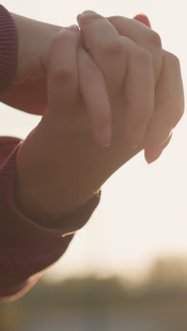 primer plano de la mano de la mujer en ropa marrón haciendo torsión de la muñeca con los dedos unidos, la luz del sol creando un efecto brillante alrededor de su mano en un entorno al aire libre pacífico