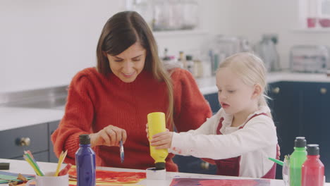 mother with daughter at home doing craft and painting picture in kitchen