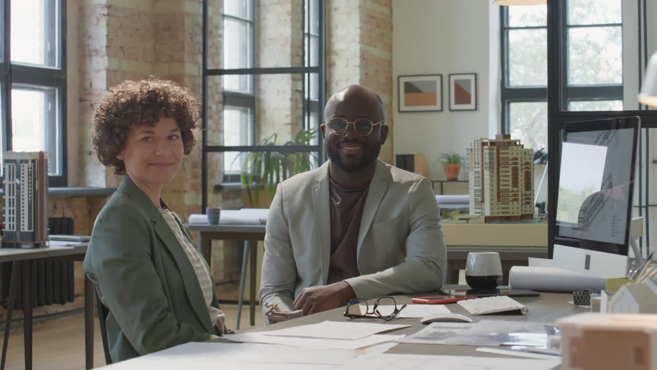 Two smiling architects in a modern office with building models and blueprints