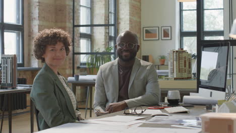 two smiling architects in a modern office with building models and blueprints