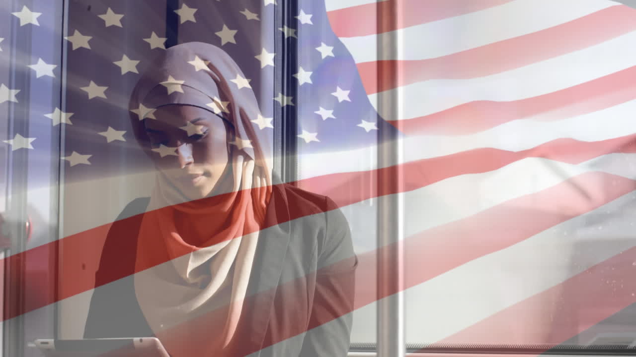 animación de la bandera estadounidense ondeando sobre una mujer biracial en hijab usando una tableta digital