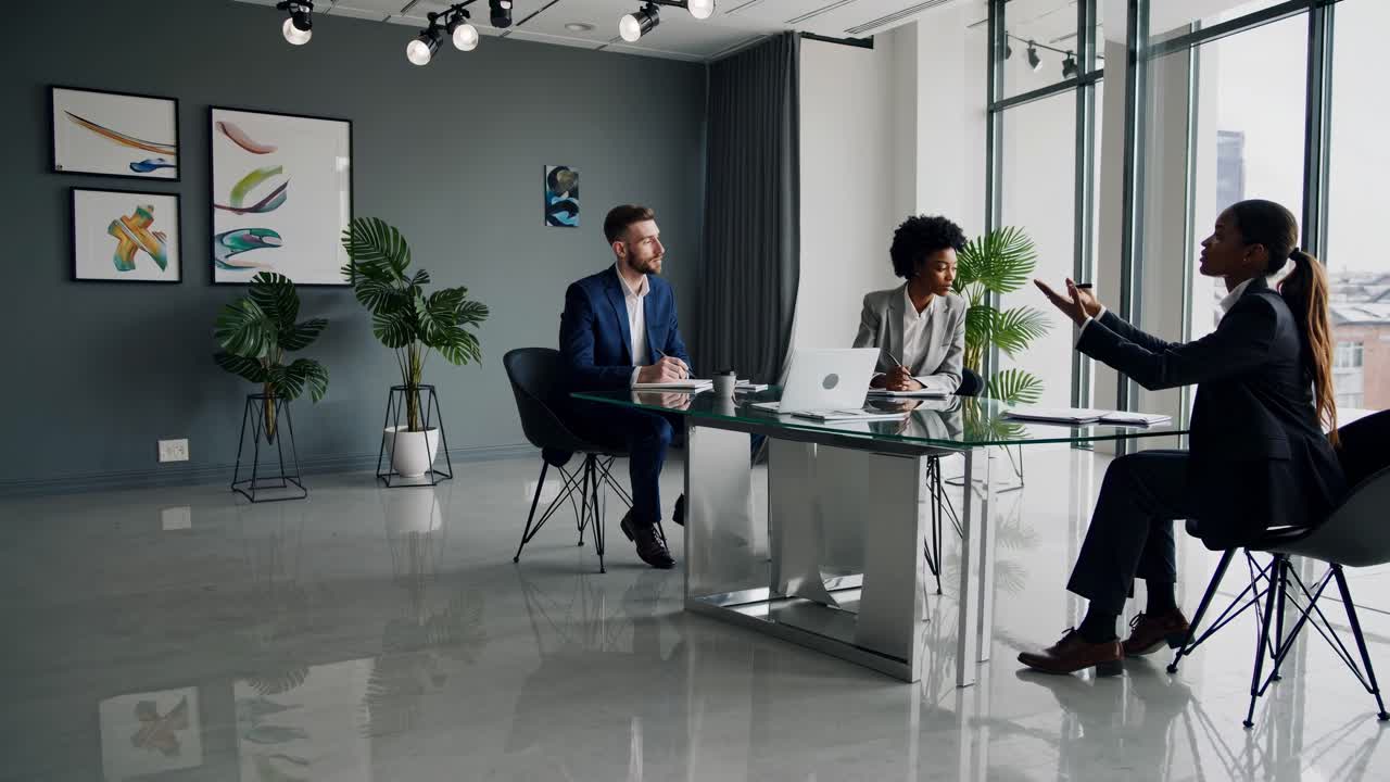 Wide-angle video shot of a modern office meeting, featuring three professionals in discussion