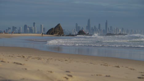 olas oceánicas en la playa y rocas currumbin - surfers paradise skyline en el fondo - currumbin alley en gold coast, queensland, australia
