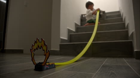 slow motion with selective focus of a young mexican latin boy playing with his car toys and a race track mounted on the stairs of his house