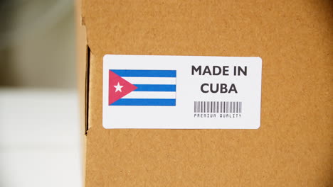 hands applying made in cuba flag label on a shipping cardboard box with products