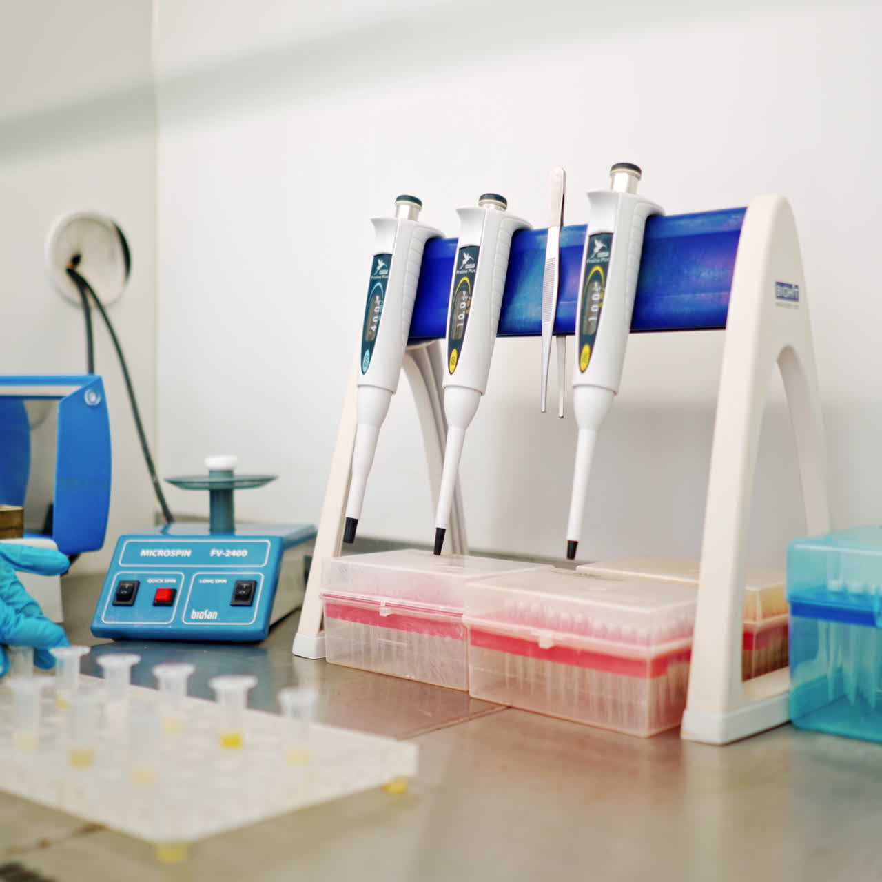 Hand of medical worker checking vials of liquid. Female's hand in sterile glove putting test tubes one by one into special machine in lab.