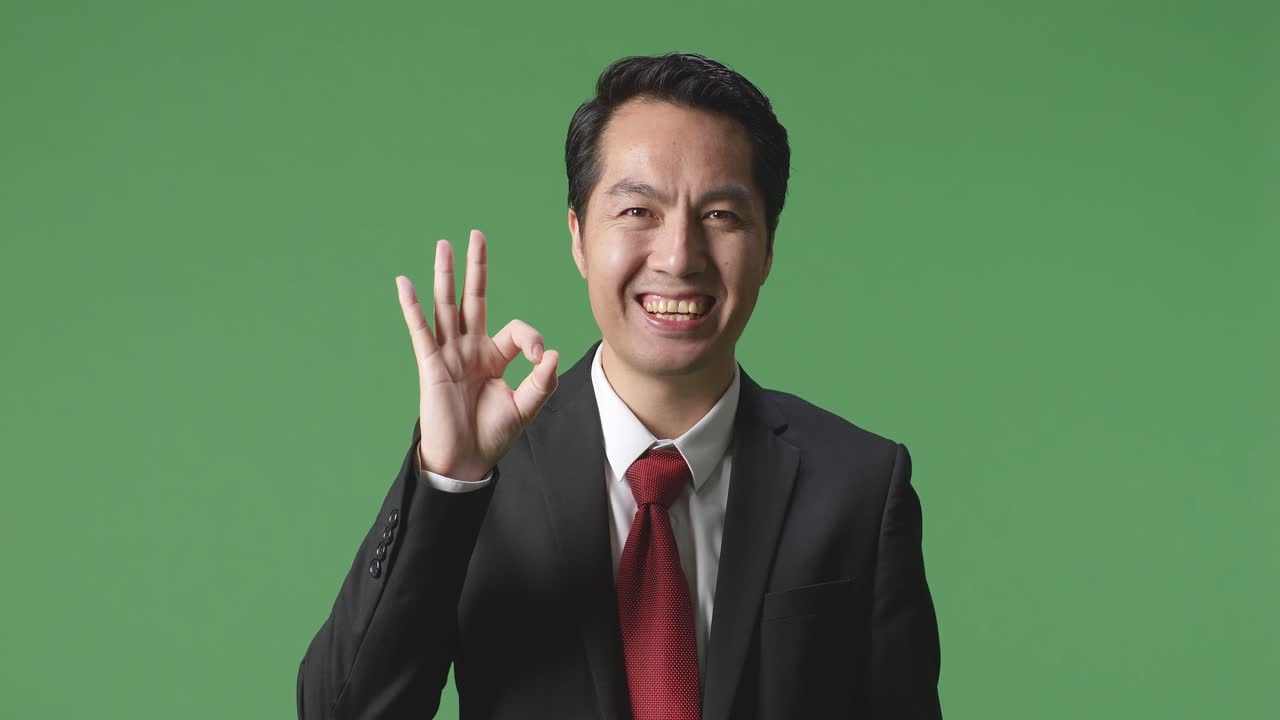 아시아 사업가 한 명 이 녹색 스크린 스튜디오 에 서 있는 동안  한 몸짓 을 하고 미소 짓고 있다