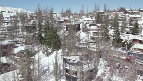 Vista-Aérea-De-Dolly-En-El-Establecimiento-Del-Pueblo-Montañoso-De-Farellones,-Cabañas-De-Lujo-Con-Materiales-Locales-Y-árboles-Con-Nieve-Y-Sin-Hojas,-Chile.