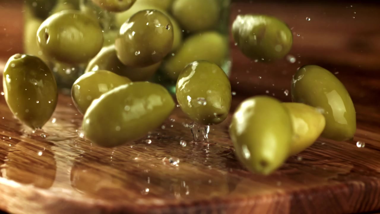 Olive verdi fresche che schizzano su una superficie di legno bagnata.
