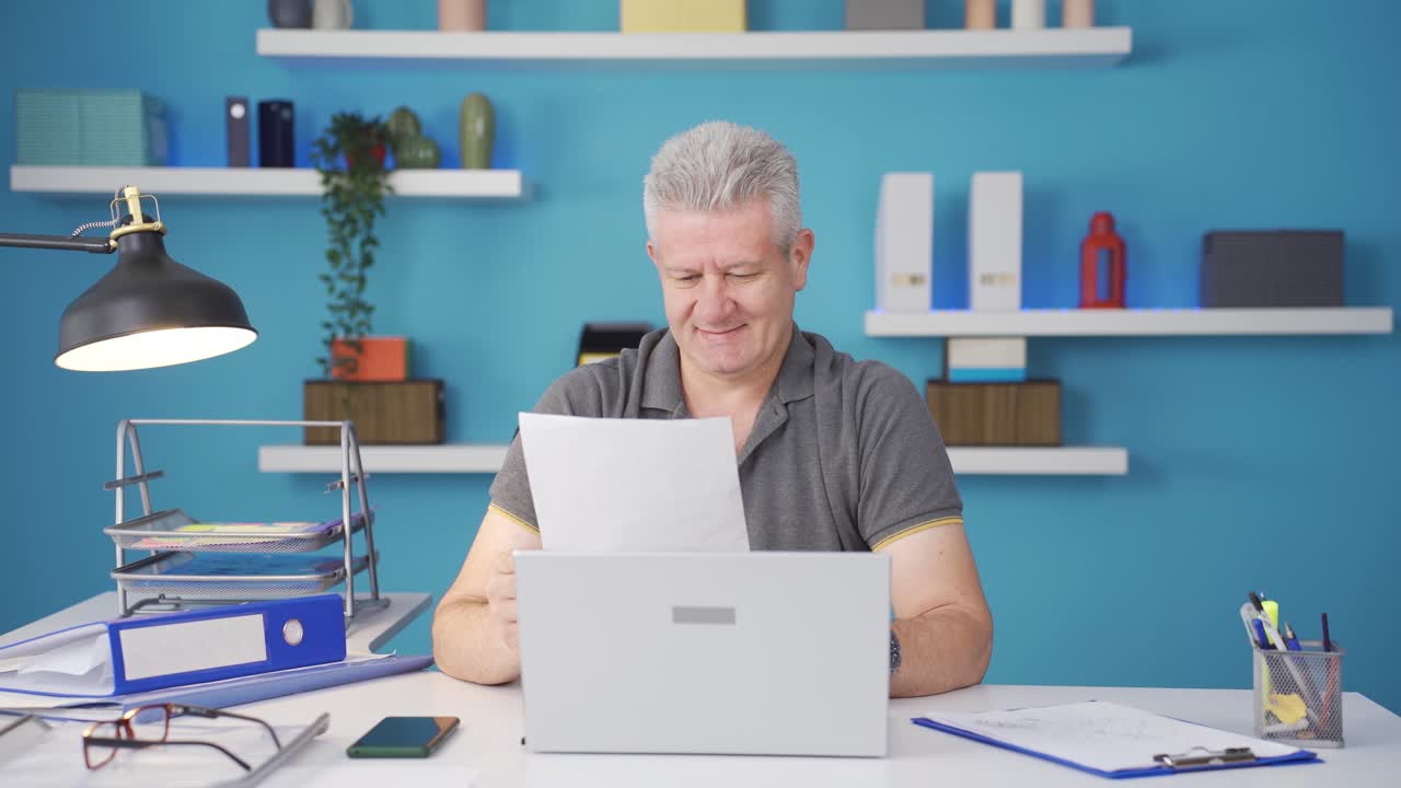 Home office worker man smiling at camera looking at paperwork.