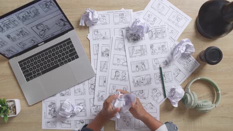 close up top view of male artist's hands crumples paper before throwing while drawing storyboard for the film on the table with a laptop and headphones in the studio