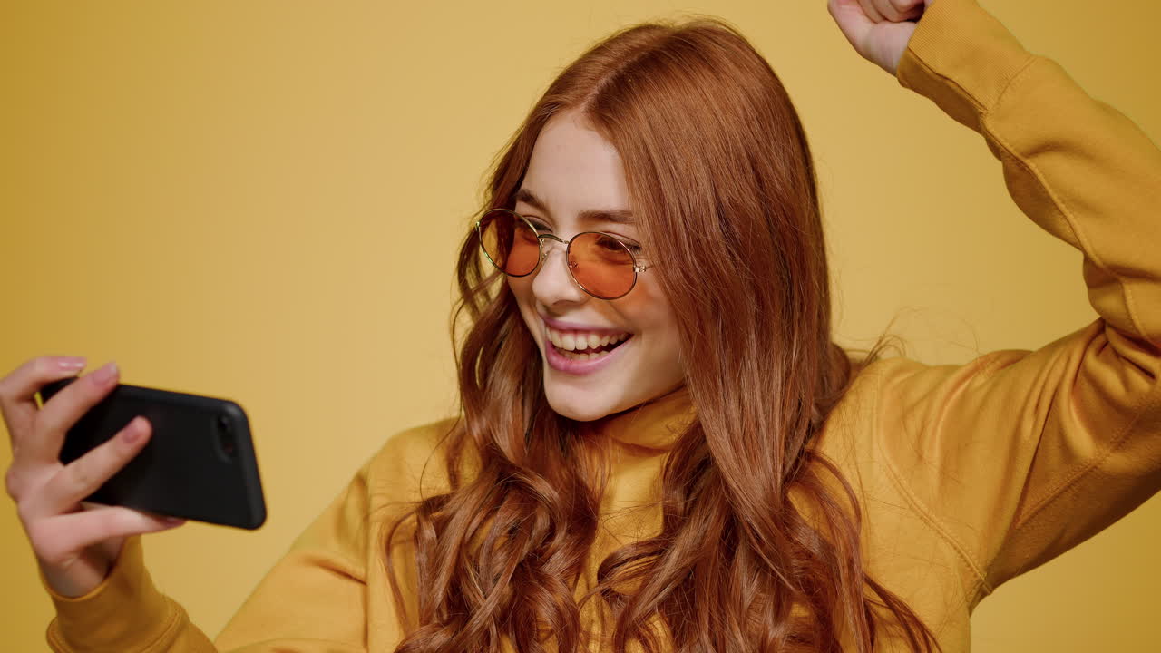 스마트폰에서 게임을 하는 행복한 여성의 초상화. 예 제스처를 보여주는 소녀