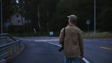 slomo shot of young man with camera walking by empty country road