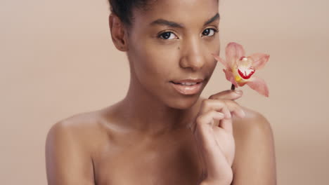 Retrato-De-Belleza-Atractiva-Mujer-Afroamericana-Posando-Juguetonamente-Con-Flor-De-Orquídea-Tocando-Una-Tez-De-Piel-Sana-Disfrutando-De-Una-Suave-Fragancia-De-Esencia-Natural-Concepto-De-Cuidado-De-La-Piel