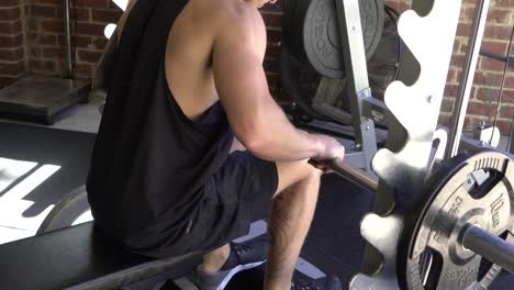 muscly man in home gym exercising smith machine calf raises while seated