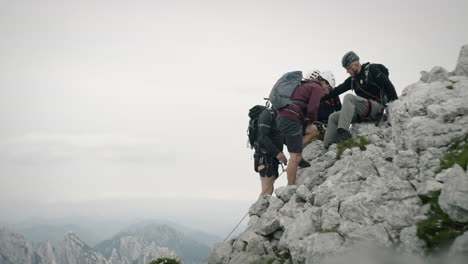 A-group-of-hikers-stops-for-a-rest-on-the-rock-in-the-moutains,-wearing-a-full-climbing-gear