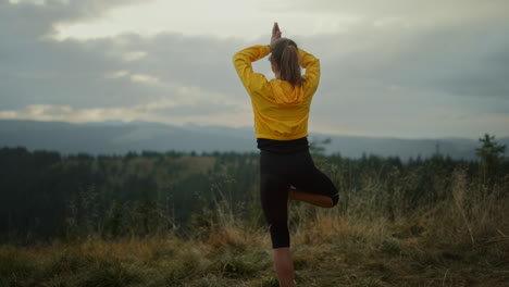 fit girl exercising yoga pose in mountains. lady standing in tree pose on grass