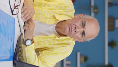 Vertical-video-of-Home-office-worker-old-man-looking-at-camera-curious-and-confused.