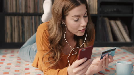 Beautiful-woman-at-home-talking-to-friend-on-smart-phone-app-on-laptop-device-lying-on-floor-relaxed-drinking-coffee