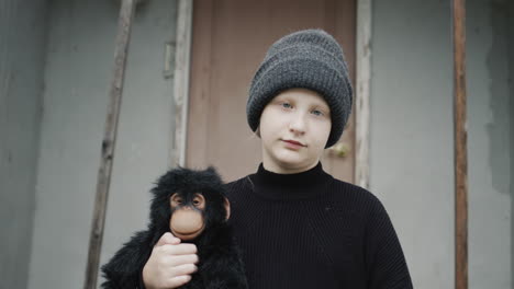 portrait of a sad girl, standing on the threshold of the house, holding a toy monkey in her hands