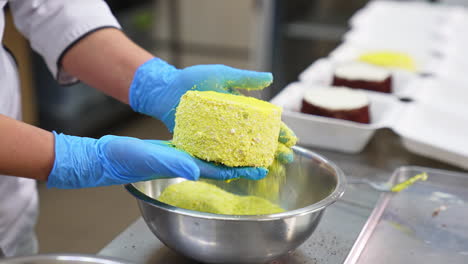 producing cakes at the confectionery. gloved hands cover yellow cake with sprinkling. factory worker puts the ready cake into individual plastic box.