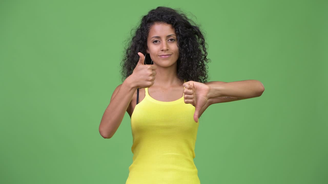 Young confused Hispanic woman choosing between thumbs up and thumbs down