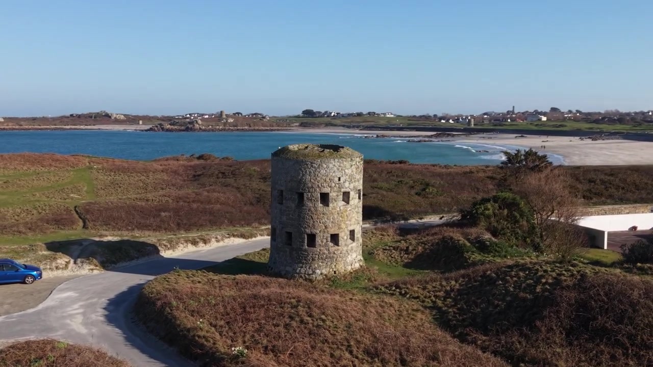 Martello Tower Pembroke Vale Guernsey. Droneflyvning kredser om Martello Tower med udsigt over Lancresse Bugt og Common i den sene eftermiddagssol med klar blå himmel.
