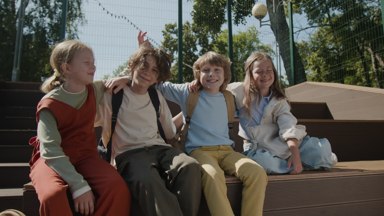 Four happy children sitting together outdoors with backpacks