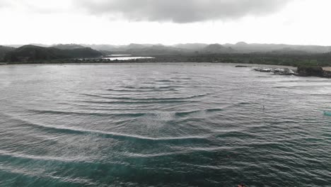 Flyover showing group of surfers gathered below and Tanjung Ana beach in the background