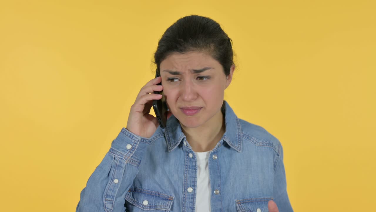 Angry Young Indian Woman Talking on Smartphone, Yellow Background