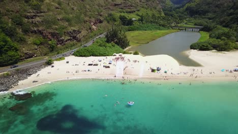 drone shot flying towards a crowd of people surrounding a slip n slide on the beach at waimea bay, hawaii