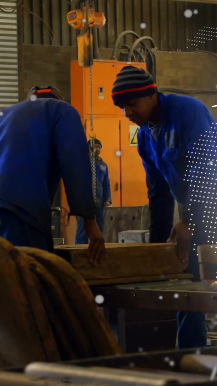Dois trabalhadores masculinos segurando e alinhando para o guindaste na fabricação, um globo varrendo obscurecendo os trabalhadores.