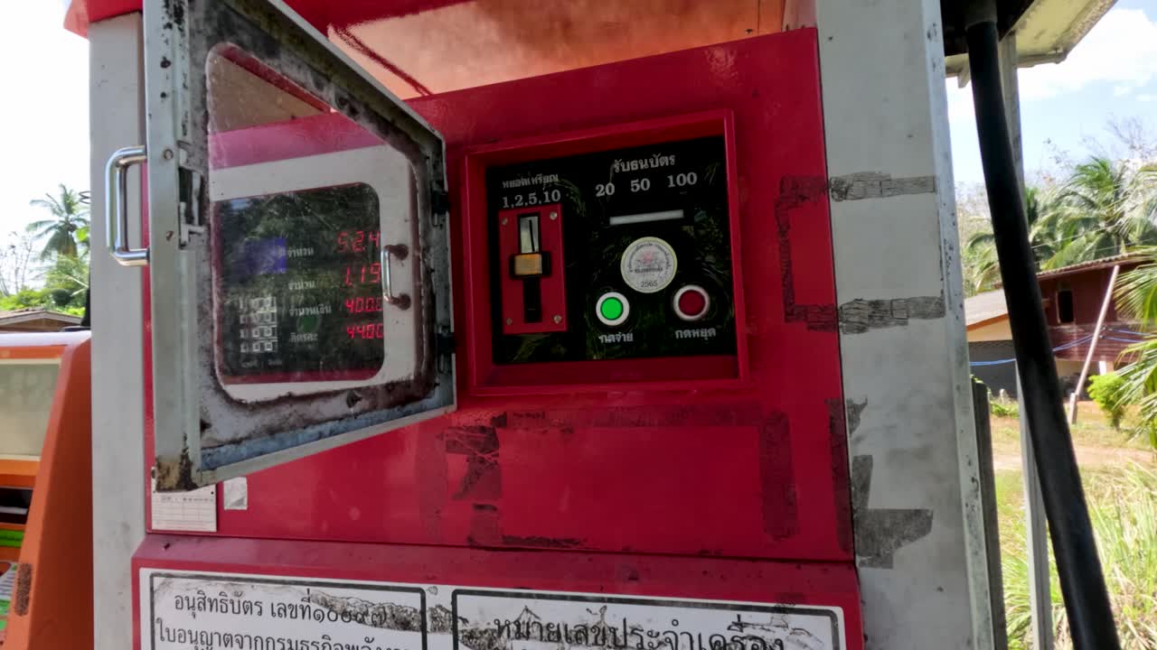 Person opens and uses red vintage fuel dispenser under bright daylight in tropical outdoor setting