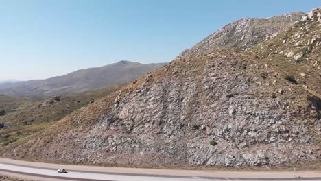 Perpendicular-aerial-flight-across-interstate-highway-beneath-dry-arid-rocky-mountain-facade-toward-countryside