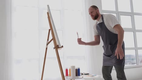 a talented artist using a brush creates a modern masterpiece of oil painting - a talented artist, using a brush, creates a modern masterpiece of oil painting. creative studio with canvas of bright colors. close-up. high quality full footage