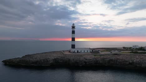 aerial fly cap d’artrutx lighthouse, southwest menorca landscape, ocean and city at dusk, sunset