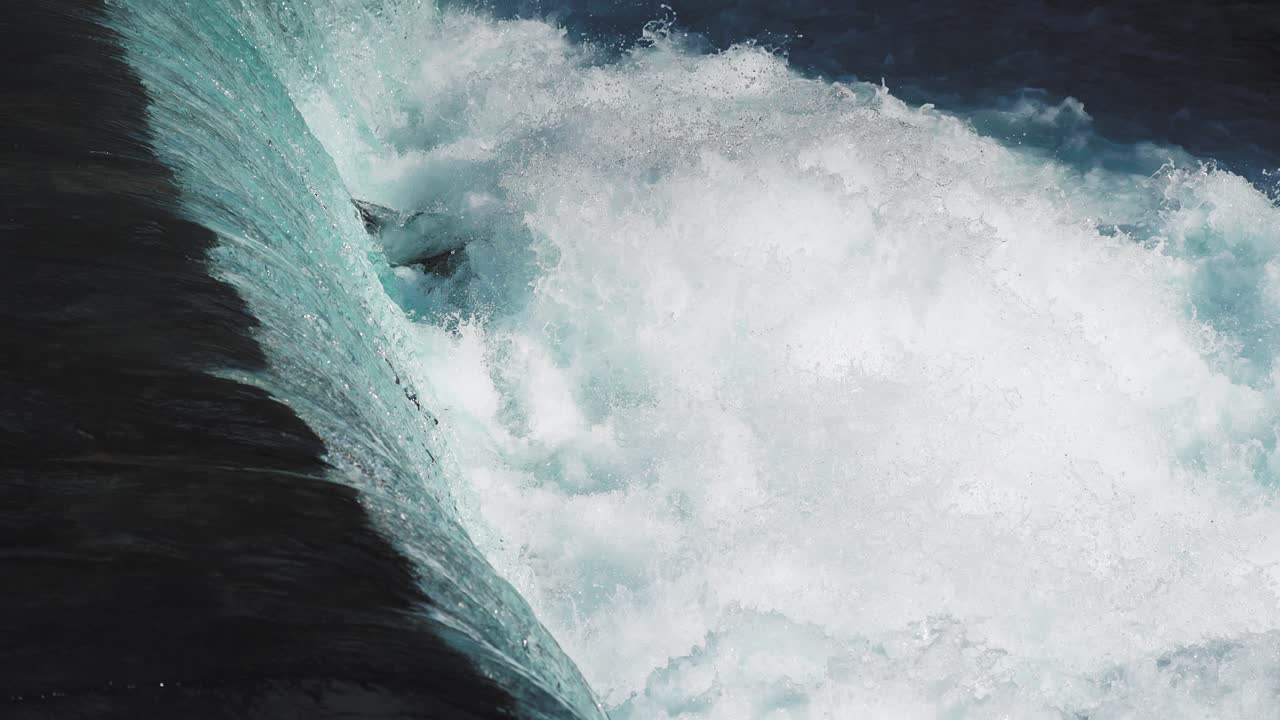 Nature footage of a waterfall, with crystal-clear water tumbling over the dark rocks, falling in the pool below whirling and foaming, creating a mesmerizing scene