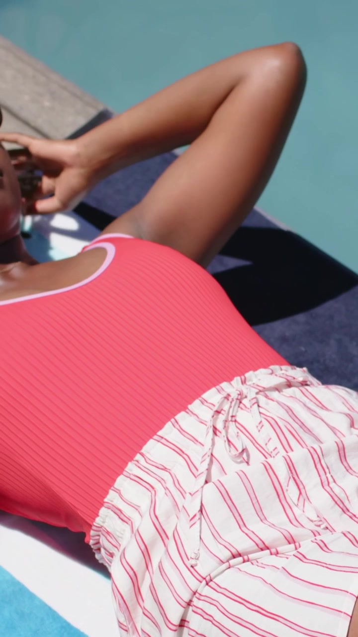 Vertical video: Panning camera showing woman adjusting sunglasses, sunbathing in ribbed swimsuit