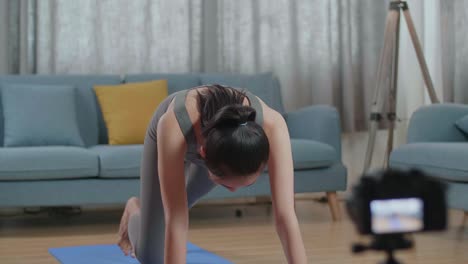 young asian trainer female speaking to camera before doing cardio high knees and core strengthening exercises while recording teaching exercise at home