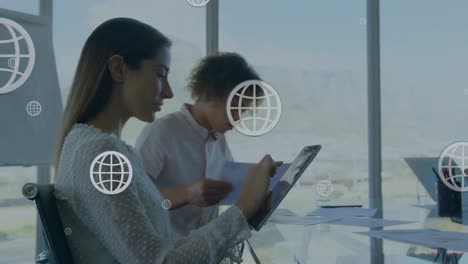 Animation-of-globe-icons-over-diverse-business-people-using-tablet