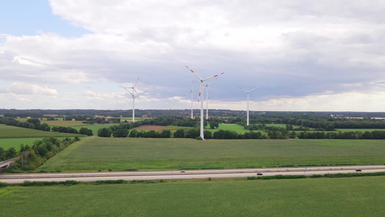 Drone footage of wind turbines beside a highway, surrounded by farmland and cornfields