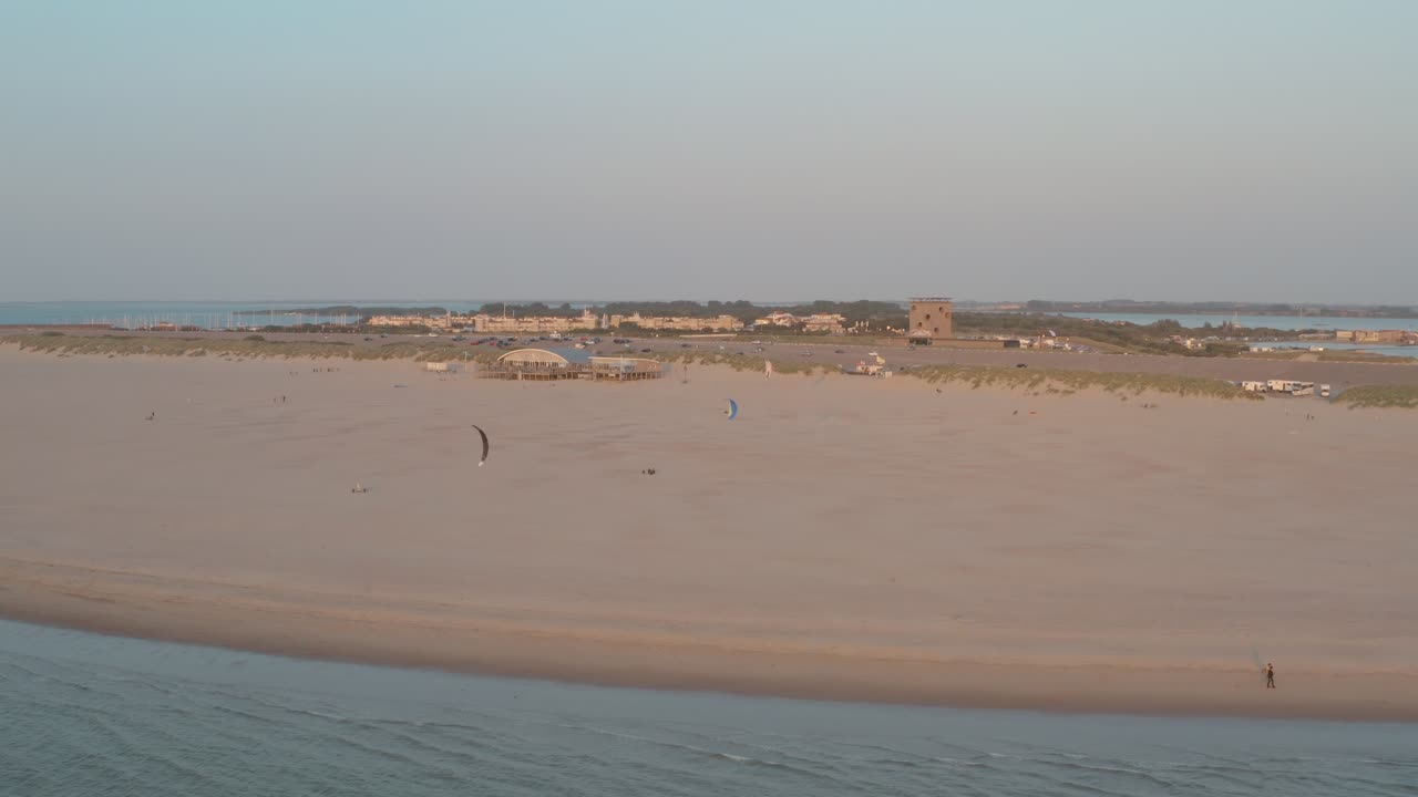 dron cinemático: panorama aéreo que rodea la playa natural verde y arenosa al atardecer con turistas y personas con buggykiting en zelanda en el mar del norte, países bajos, 25p