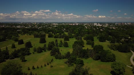 An-aerial-drone-shot-over-Maisonneuve-park-in-Montreal,-blue-sky,-green-trees,-tilt-down