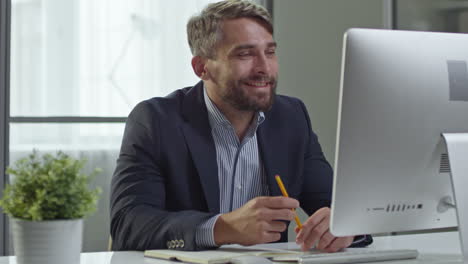 businessman in striped shirt and jacket with gray hair sitting in front of the computer while speaking in an online meeting