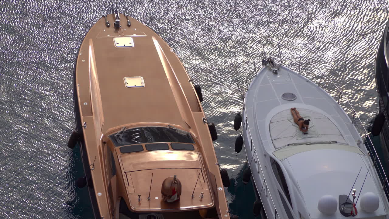Fontvieille, Monaco - July 4, 2025: Close-up of luxury yachts docked in the marina, with a woman sunbathing on the deck
