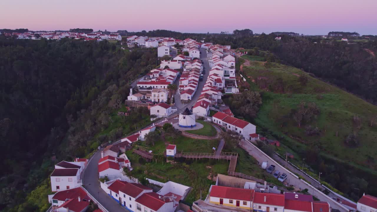 Vista aérea de Odeceixe com moinho de vento, aldeia tradicional, mostrando um cenário histórico sereno em Portugal.
