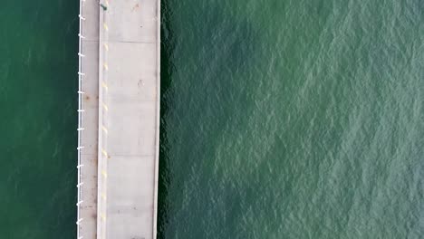 aerial - birds eye drone shot of couple walking along bridge over green water