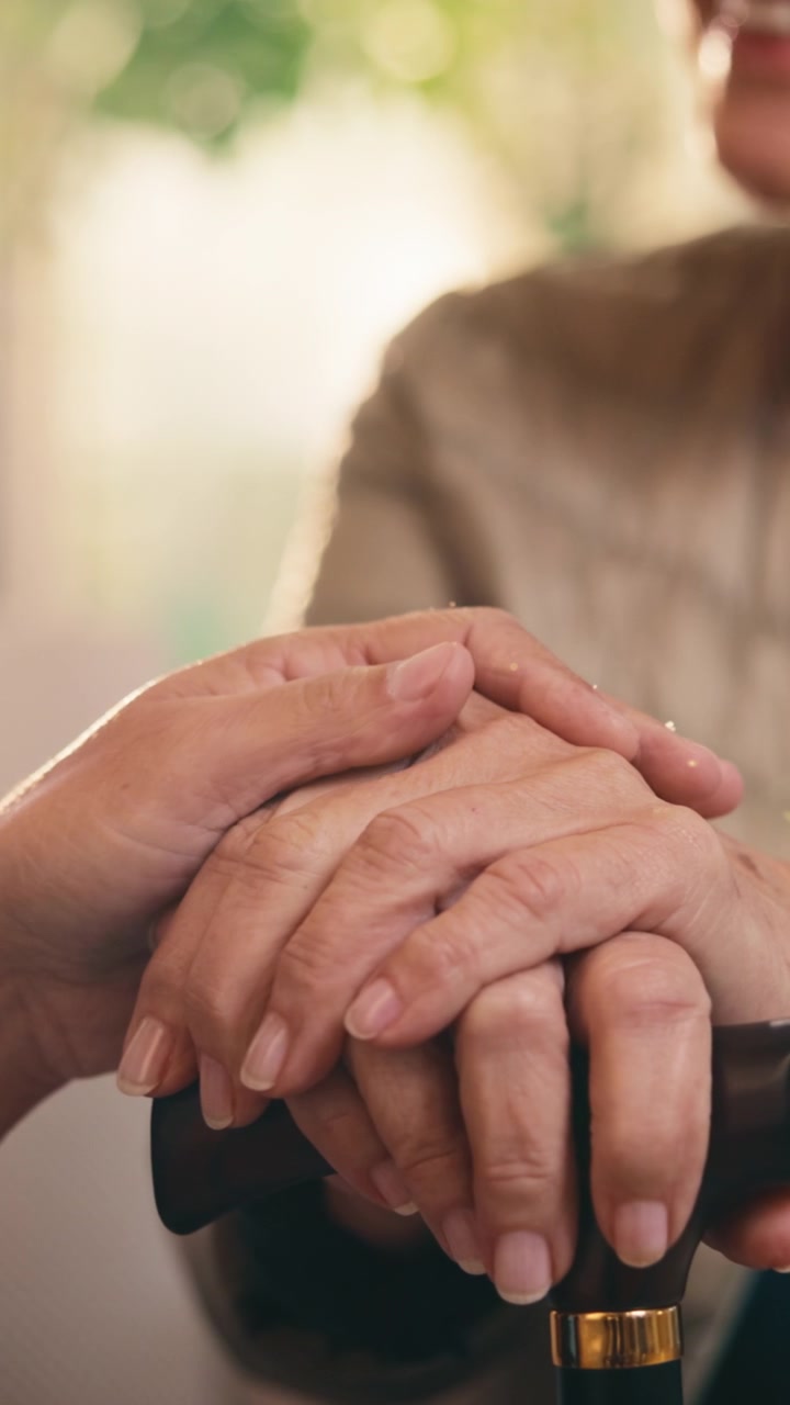 Primer plano de una persona sosteniendo las manos de una mujer mayor con bastón